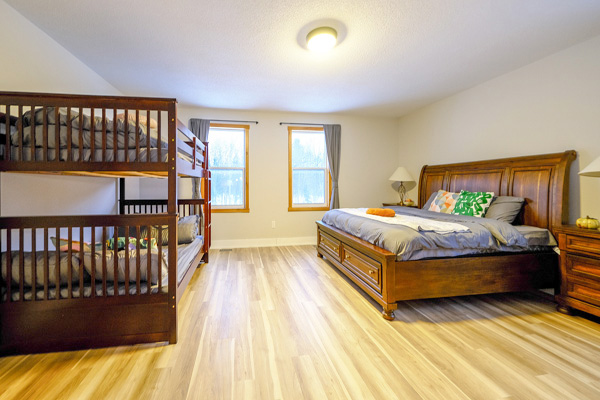 Living room with wooden walls, large windows, dark leather sectional sofa, and glass coffee table.